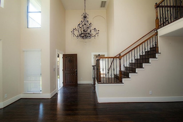 entryway featuring a towering ceiling, dark wood-type flooring, and a notable chandelier