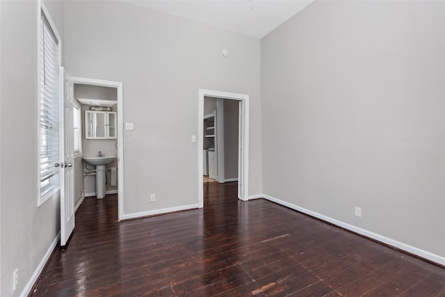 unfurnished bedroom with ensuite bath, sink, a high ceiling, dark hardwood / wood-style floors, and a walk in closet