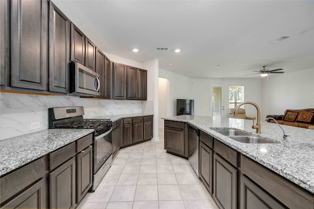 kitchen featuring stainless steel appliances, dark brown cabinetry, sink, light tile patterned floors, and backsplash