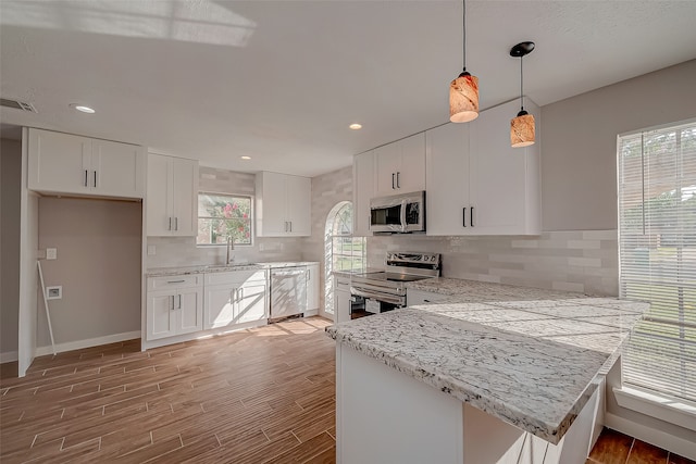 kitchen with white cabinets, stainless steel appliances, hanging light fixtures, and sink