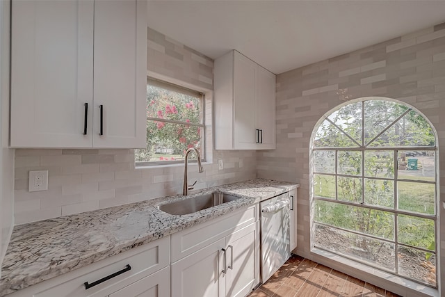 kitchen with white cabinetry, sink, light stone countertops, stainless steel dishwasher, and decorative backsplash