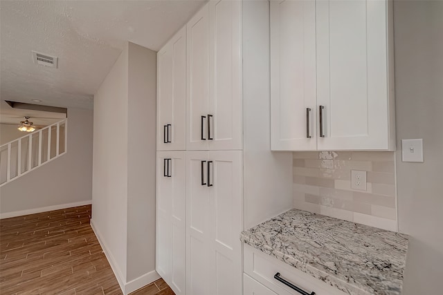 kitchen with light stone counters, a textured ceiling, light hardwood / wood-style flooring, white cabinets, and decorative backsplash