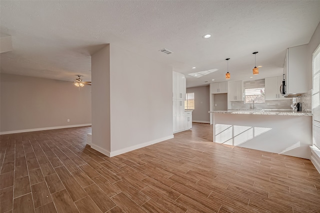 unfurnished living room with light wood-type flooring, a textured ceiling, ceiling fan, and sink