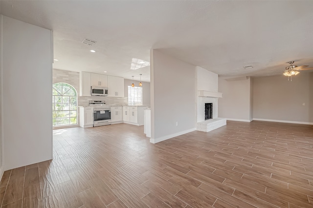 unfurnished living room featuring a brick fireplace, light hardwood / wood-style floors, and ceiling fan