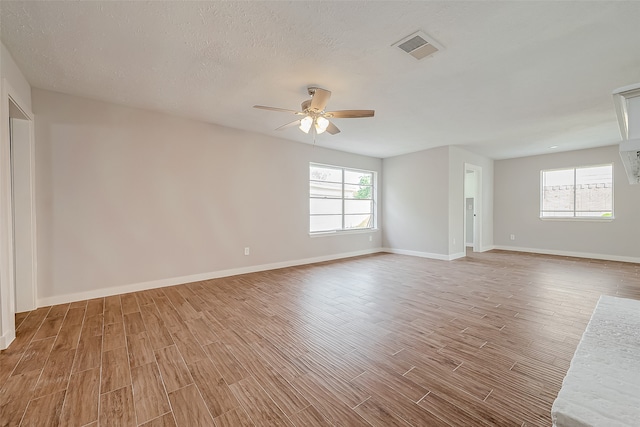 empty room with a textured ceiling, hardwood / wood-style floors, and a healthy amount of sunlight