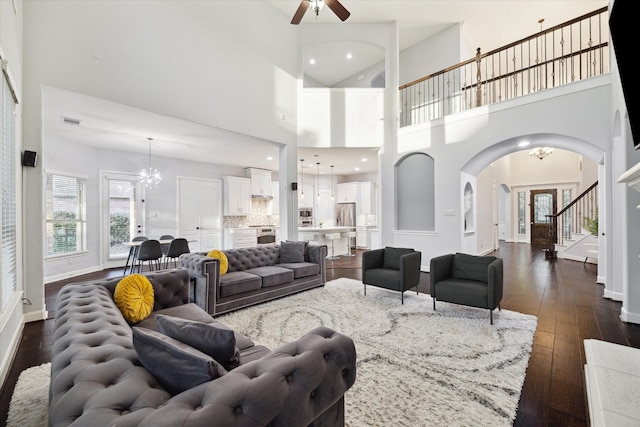 living room featuring dark hardwood / wood-style flooring, ceiling fan with notable chandelier, a healthy amount of sunlight, and a towering ceiling