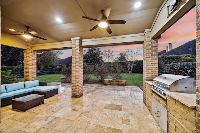 patio terrace at dusk with ceiling fan, an outdoor kitchen, area for grilling, and outdoor lounge area