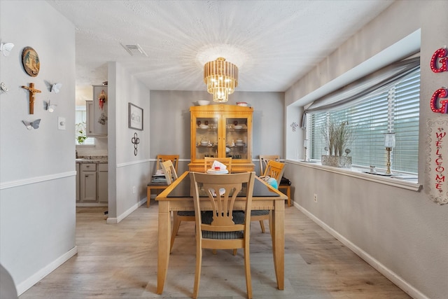 dining room with light wood-type flooring, visible vents, baseboards, and a notable chandelier