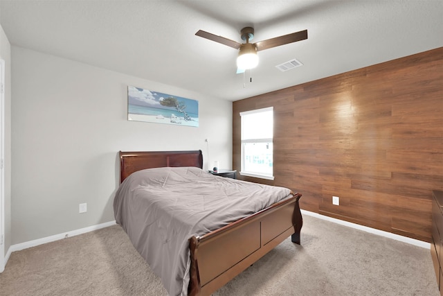 carpeted bedroom featuring wood walls and ceiling fan