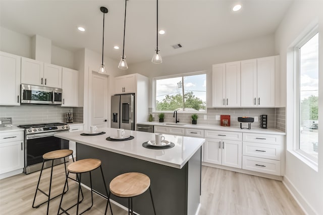 kitchen with stainless steel appliances, white cabinetry, decorative backsplash, sink, and a center island