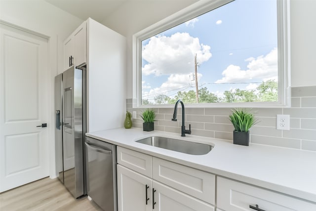 kitchen with tasteful backsplash, stainless steel appliances, white cabinetry, sink, and light hardwood / wood-style floors