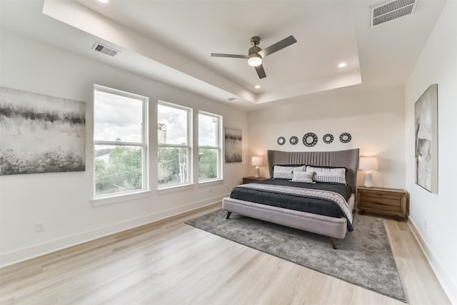 bedroom featuring light wood-type flooring, ceiling fan, and a raised ceiling