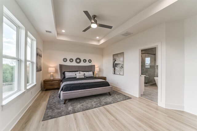 bedroom with light wood-type flooring, ceiling fan, a raised ceiling, and connected bathroom