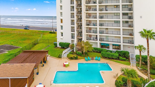 view of swimming pool featuring a view of the beach, a water view, a lawn, and a patio