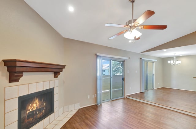 unfurnished living room featuring a tile fireplace, ceiling fan with notable chandelier, light hardwood / wood-style flooring, and vaulted ceiling