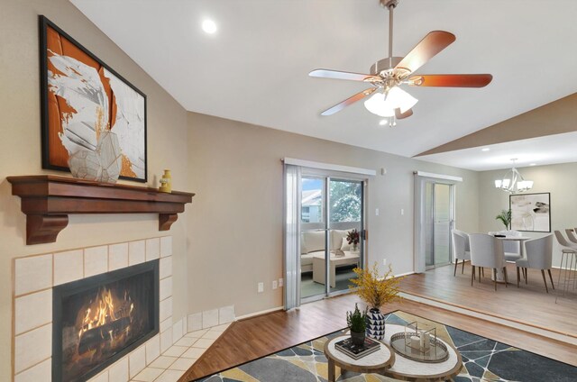 living room with ceiling fan with notable chandelier, a tiled fireplace, lofted ceiling, and light hardwood / wood-style flooring