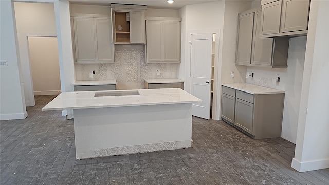 kitchen with gray cabinets, dark hardwood / wood-style floors, a center island, and backsplash