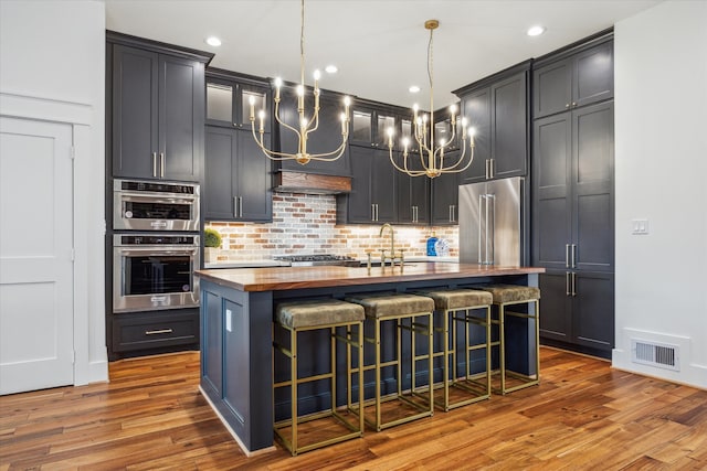 kitchen featuring butcher block counters, appliances with stainless steel finishes, a kitchen breakfast bar, an island with sink, and hardwood / wood-style floors