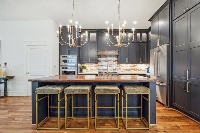 kitchen with stainless steel appliances, butcher block counters, a center island, a breakfast bar area, and light hardwood / wood-style flooring