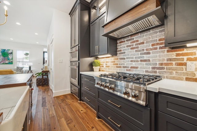 kitchen featuring stainless steel gas cooktop, custom range hood, and light hardwood / wood-style flooring