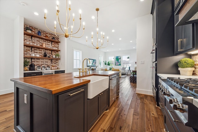 kitchen with wooden counters, dark hardwood / wood-style flooring, hanging light fixtures, sink, and a kitchen island with sink