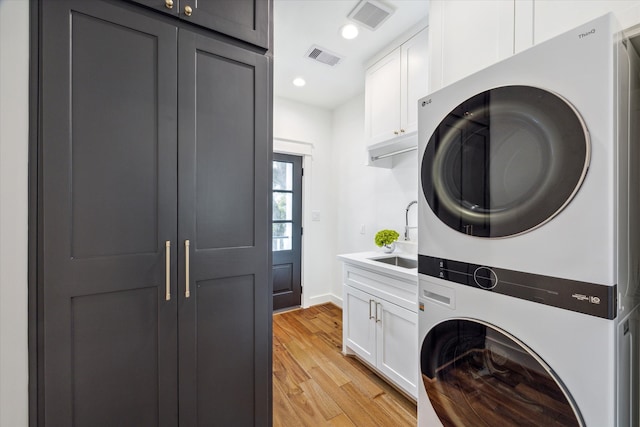 laundry room featuring stacked washer / dryer, cabinets, sink, and light hardwood / wood-style floors