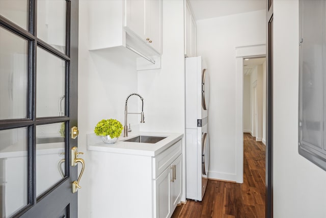 laundry room with dark wood-type flooring, stacked washing maching and dryer, and sink