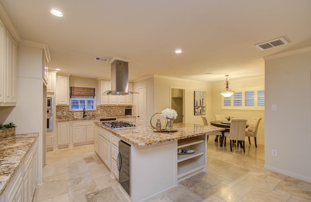 kitchen with light stone counters, decorative light fixtures, ventilation hood, stainless steel gas stovetop, and a kitchen island