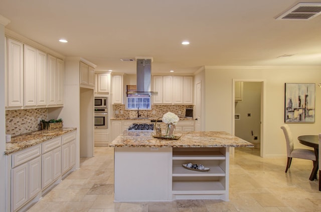 kitchen featuring wall chimney range hood, tasteful backsplash, light stone counters, and a center island