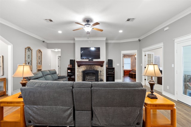 living room featuring hardwood / wood-style floors, a stone fireplace, ceiling fan, and ornamental molding