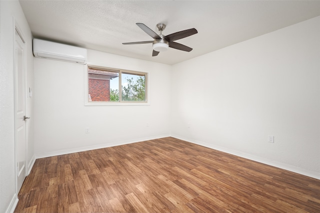 empty room with a textured ceiling, hardwood / wood-style flooring, an AC wall unit, and ceiling fan