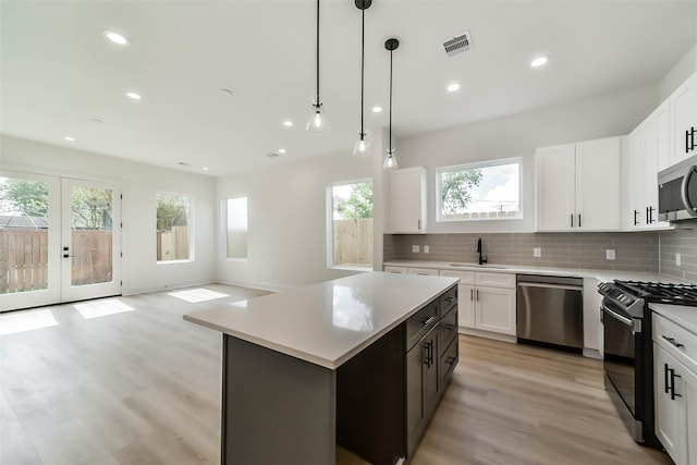 kitchen featuring stainless steel appliances, light hardwood / wood-style floors, hanging light fixtures, a center island, and white cabinets