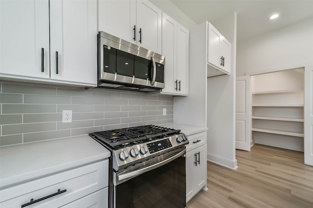 kitchen featuring white cabinets, light wood-type flooring, appliances with stainless steel finishes, and backsplash