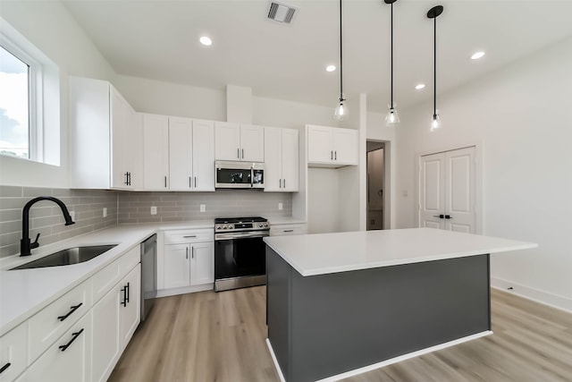 kitchen featuring sink, appliances with stainless steel finishes, decorative light fixtures, a center island, and white cabinets