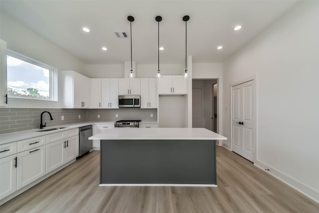 kitchen featuring white cabinetry, appliances with stainless steel finishes, hanging light fixtures, a center island, and light wood-type flooring