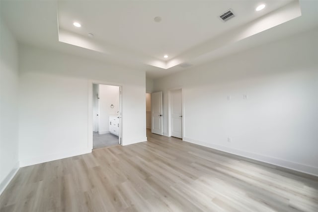 unfurnished bedroom featuring light wood-type flooring, ensuite bath, and a tray ceiling