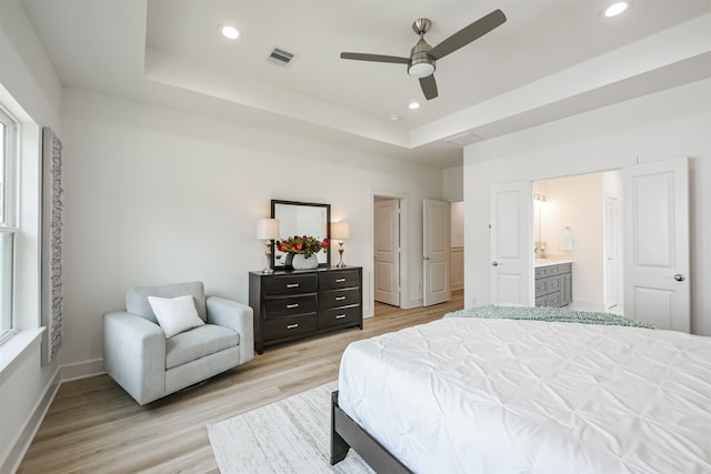 bedroom featuring light hardwood / wood-style flooring, a raised ceiling, ceiling fan, and ensuite bath