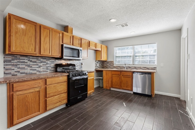 kitchen featuring sink, dark hardwood / wood-style floors, a textured ceiling, appliances with stainless steel finishes, and tasteful backsplash