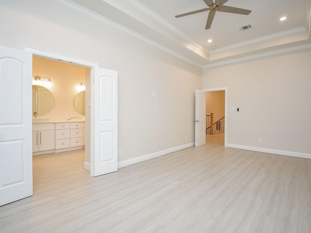 unfurnished bedroom featuring ensuite bathroom, a raised ceiling, light hardwood / wood-style flooring, and crown molding