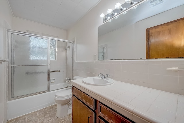 full bathroom featuring tile patterned floors, toilet, tile walls, bath / shower combo with glass door, and vanity