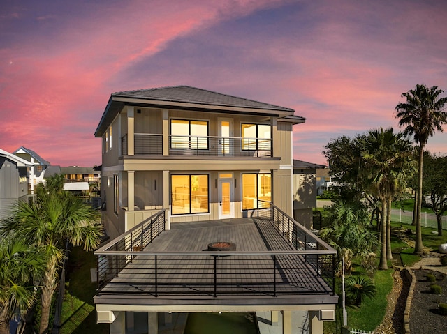 back of house at dusk featuring a balcony and stucco siding