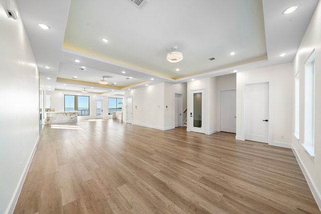 unfurnished living room featuring recessed lighting, visible vents, baseboards, light wood-style floors, and a raised ceiling