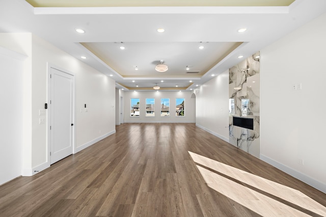 unfurnished living room featuring a raised ceiling, wood finished floors, and recessed lighting