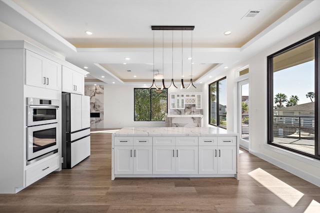 kitchen with white appliances, visible vents, a tray ceiling, and wood finished floors