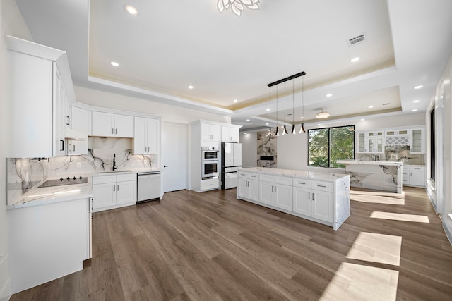 kitchen with decorative light fixtures, white cabinetry, and a tray ceiling