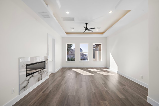 unfurnished living room featuring dark hardwood / wood-style floors, ceiling fan, and a tray ceiling