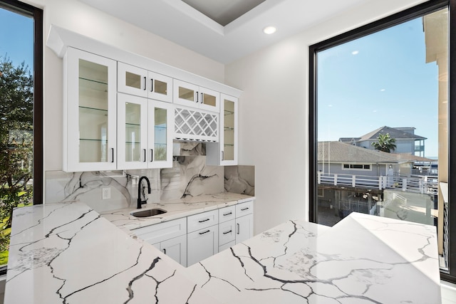 kitchen with backsplash, light stone counters, white cabinetry, and sink