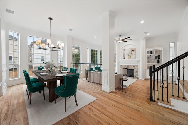 dining space with built in shelves, light hardwood / wood-style floors, a fireplace, and ceiling fan with notable chandelier