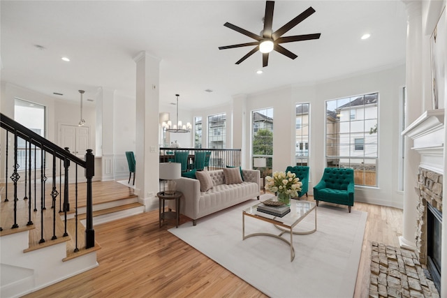 living room featuring a fireplace, ceiling fan with notable chandelier, light hardwood / wood-style floors, and ornamental molding