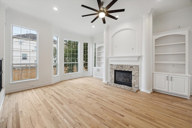 unfurnished living room with ceiling fan, built in features, crown molding, a fireplace, and light wood-type flooring